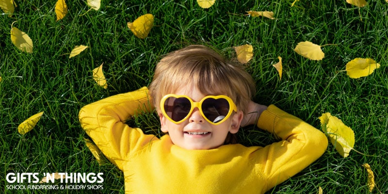 child laying on grass smiling with yellow heart-shaped sunglasses